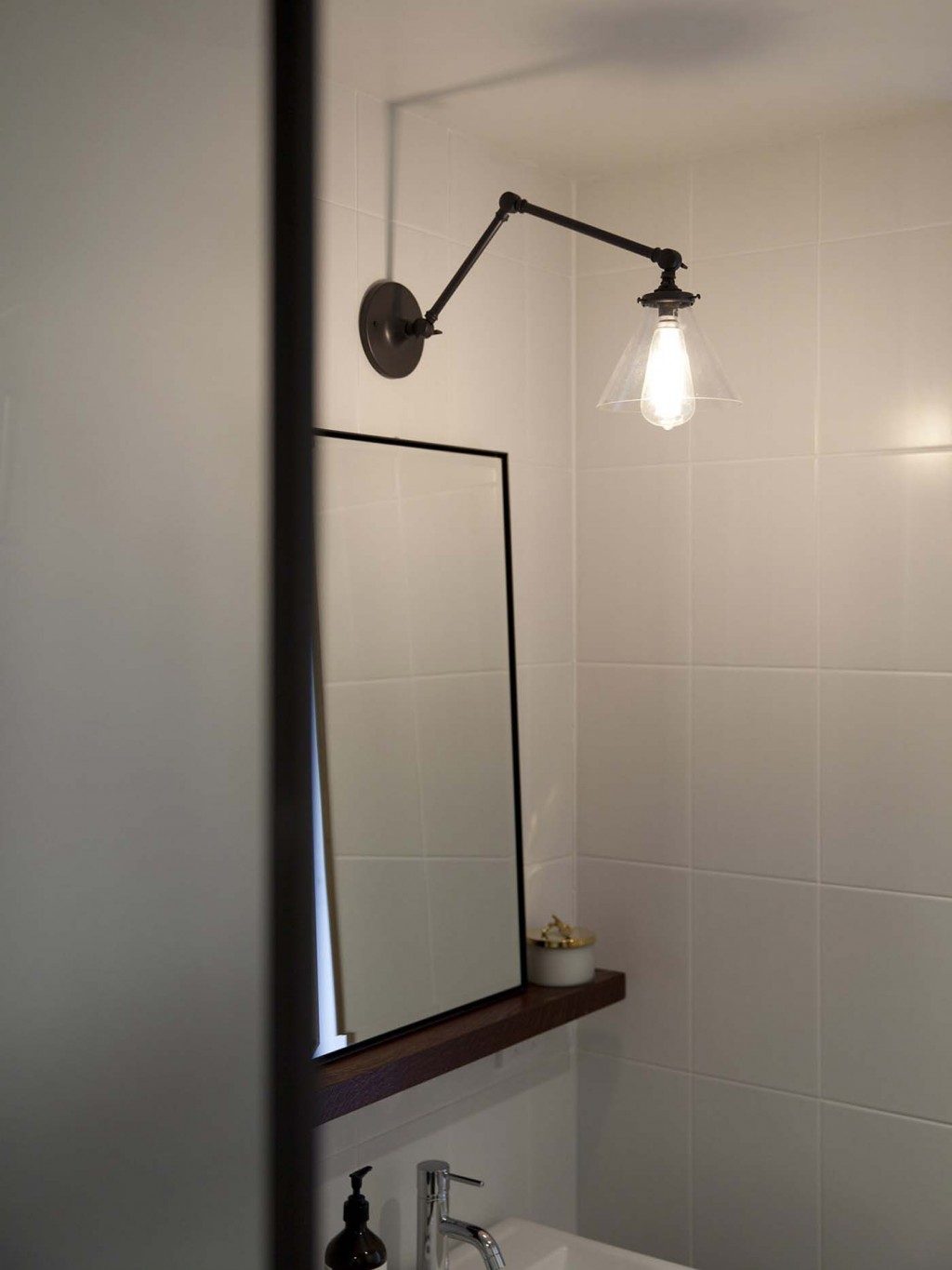 A Princeton 'Senior' wall sconce from Schoolhouse Electric is fixed to the wall above a simple wooden shelf holding a mirror custom-designed by Carroll. Photograph by David Straight.