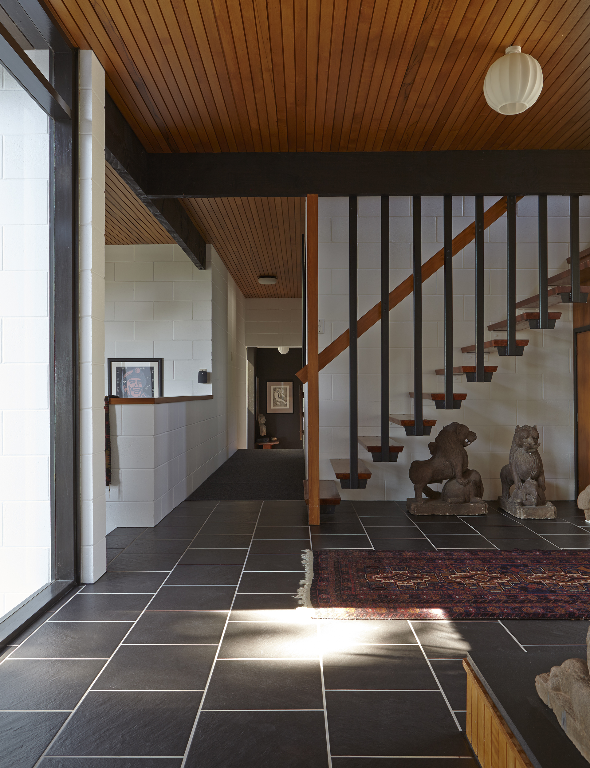 The artwork at the end of the hall is ‘Romeo and Juliet’ by Arthur Boyd. To the left of the low landing wall is ‘The Belief II’ by Wang Guangyi. Two antique temple lions stand guard inside the entrance to the home. An antique rug is placed in the entrance.