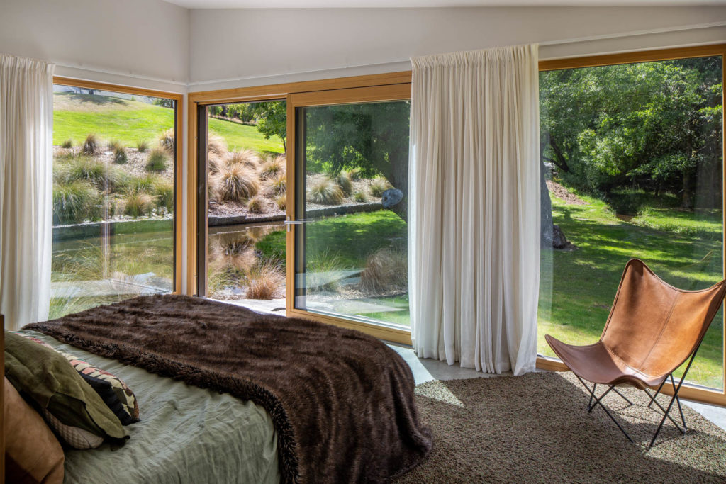 A view of the bedroom to the outside garden. A lot of greenery, a pond, and large open windows and doors.